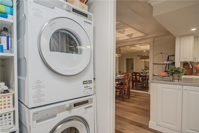 clothes washing area with light wood-type flooring, ornamental molding, and stacked washer and dryer