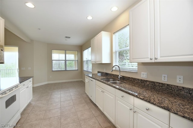 kitchen featuring stove, white cabinetry, dark stone countertops, and sink