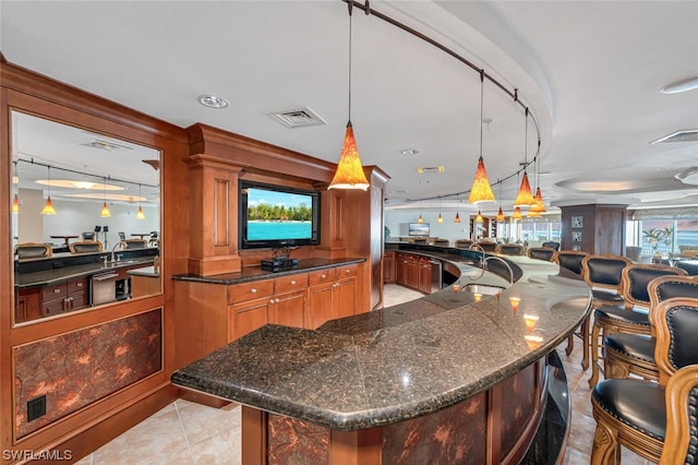 kitchen with decorative light fixtures, light tile flooring, dark stone countertops, a center island with sink, and a breakfast bar area