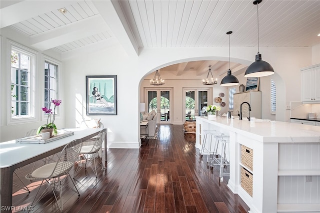 kitchen with vaulted ceiling with beams, hanging light fixtures, a center island with sink, white cabinetry, and dark hardwood / wood-style floors