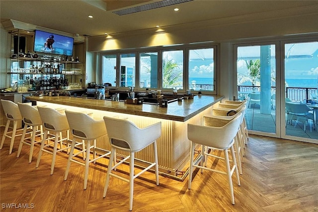 bar with light parquet floors, a water view, and a healthy amount of sunlight