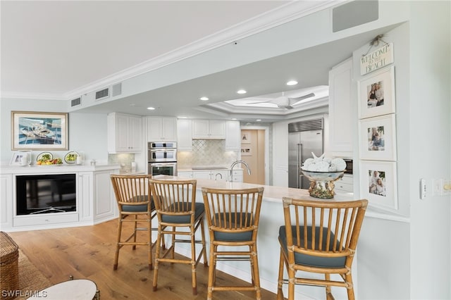 dining space with light hardwood / wood-style floors, a tray ceiling, sink, and ornamental molding