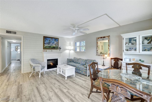 living room with ceiling fan, light hardwood / wood-style floors, a textured ceiling, and wood walls