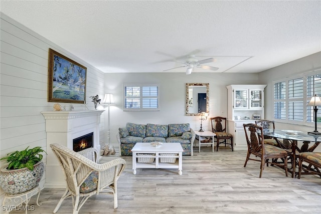 living room featuring ceiling fan, a textured ceiling, light hardwood / wood-style flooring, and wood walls