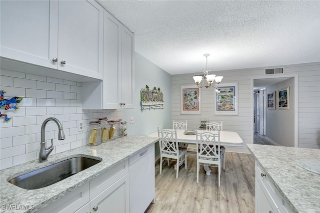 kitchen featuring white dishwasher, sink, hanging light fixtures, and white cabinets