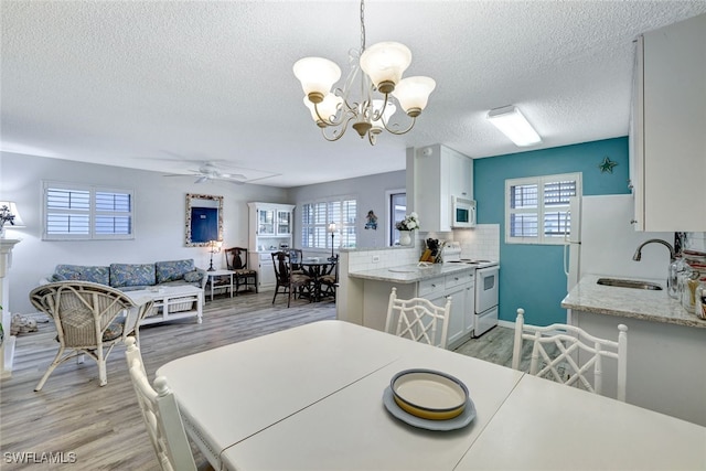 dining area with sink, ceiling fan with notable chandelier, a textured ceiling, and light hardwood / wood-style flooring