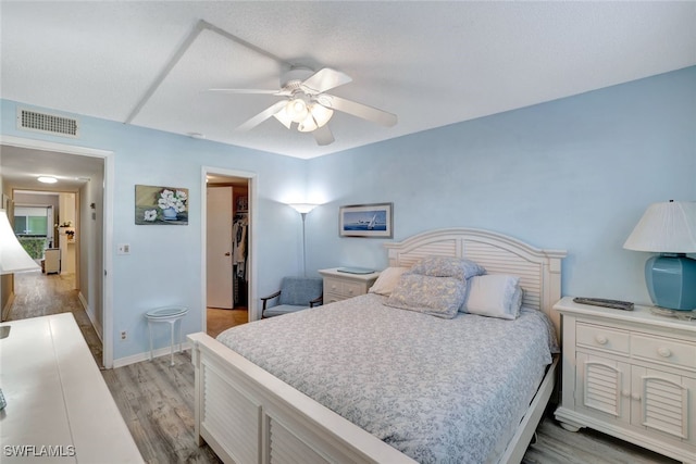 bedroom with ceiling fan, a walk in closet, a closet, and light hardwood / wood-style floors