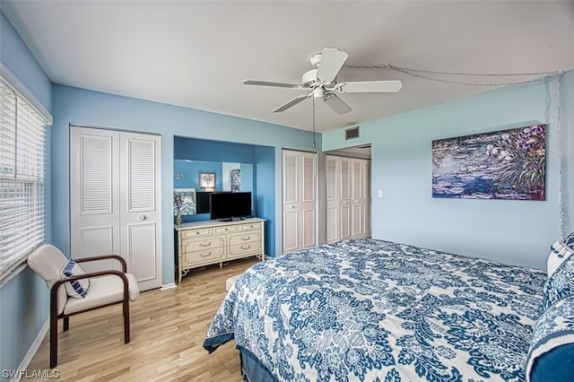 bedroom with two closets, light hardwood / wood-style floors, and ceiling fan