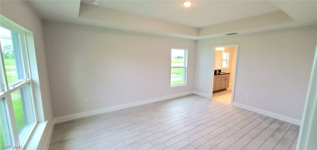 unfurnished bedroom featuring light wood-type flooring, a tray ceiling, and connected bathroom