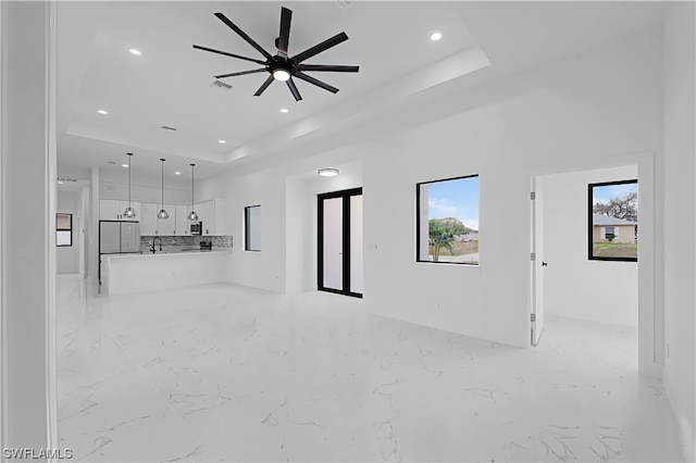 unfurnished living room featuring a tray ceiling, ceiling fan, and light tile flooring