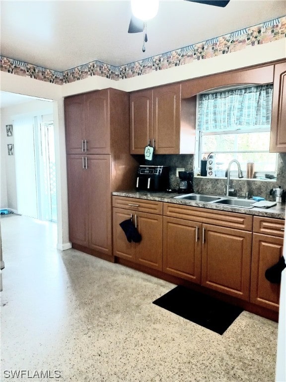 kitchen featuring backsplash, light stone counters, ceiling fan, and sink