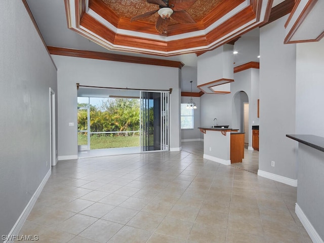 unfurnished living room with plenty of natural light, a raised ceiling, light tile floors, and ceiling fan with notable chandelier