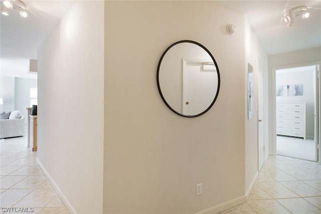 corridor featuring light tile patterned floors, baseboards, and rail lighting