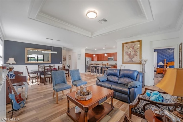 living room with a raised ceiling, light hardwood / wood-style floors, and ornamental molding