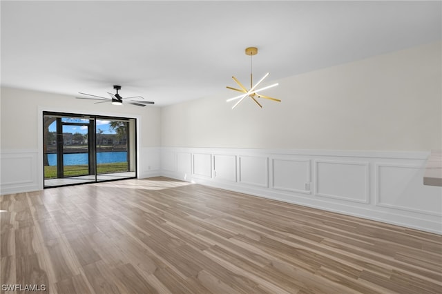 empty room with a water view, ceiling fan with notable chandelier, and light hardwood / wood-style flooring