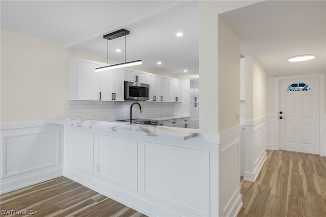 kitchen with kitchen peninsula, white cabinets, backsplash, decorative light fixtures, and light wood-type flooring