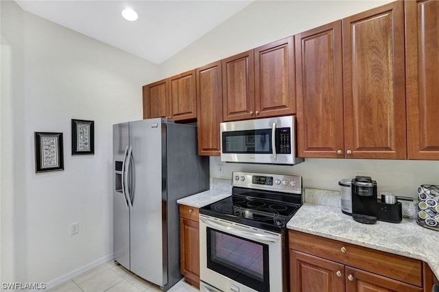 kitchen with appliances with stainless steel finishes, vaulted ceiling, light stone countertops, and light tile flooring