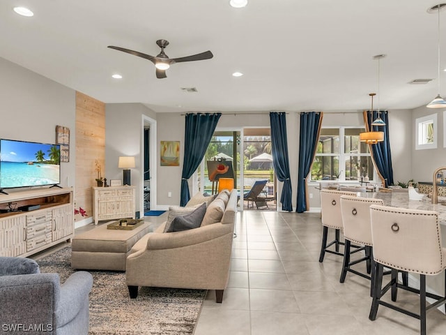 living room featuring wooden walls, light tile flooring, a healthy amount of sunlight, and ceiling fan