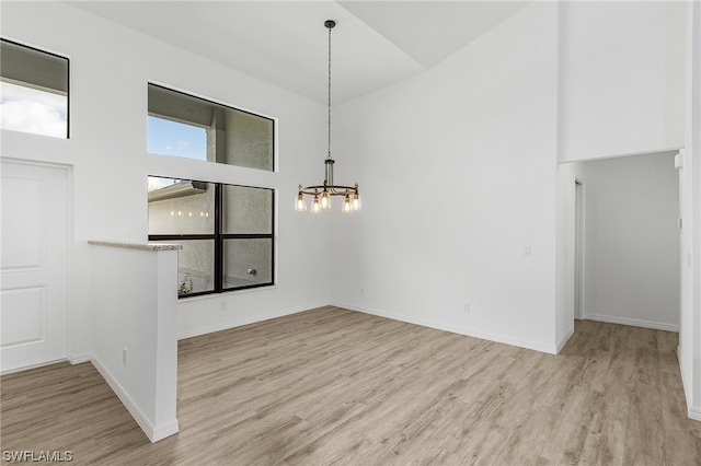 empty room featuring a high ceiling, a notable chandelier, and light hardwood / wood-style floors