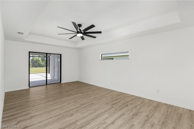 spare room with a raised ceiling, ceiling fan, and light wood-type flooring