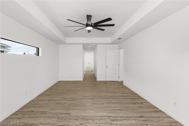 spare room with a tray ceiling, ceiling fan, and light wood-type flooring