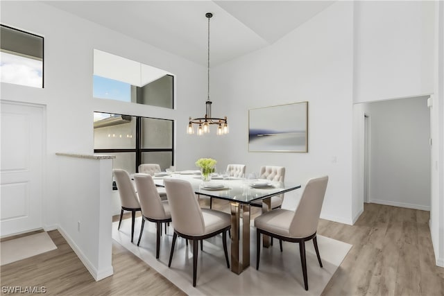 dining room featuring an inviting chandelier, light hardwood / wood-style floors, and a towering ceiling