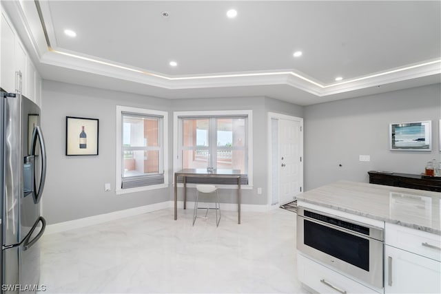 kitchen with stainless steel fridge, light tile flooring, light stone countertops, white cabinets, and a tray ceiling