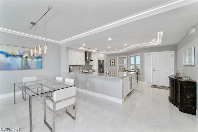 kitchen with stainless steel fridge, light tile floors, decorative light fixtures, wall chimney range hood, and white cabinets