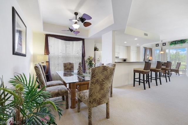 dining room with light colored carpet, a tray ceiling, and ceiling fan