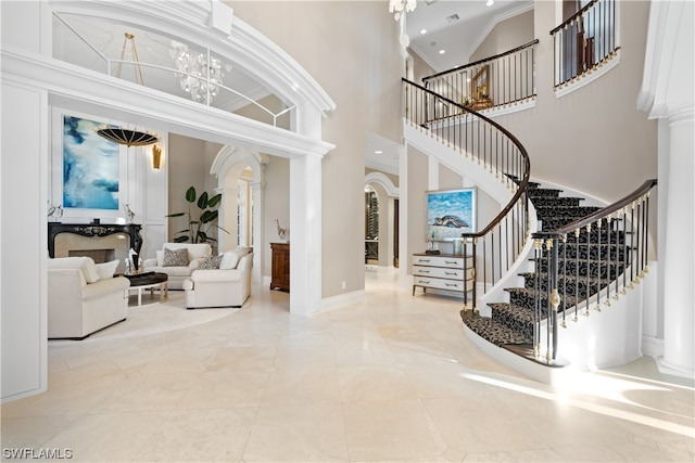 tiled entrance foyer with decorative columns, an inviting chandelier, a towering ceiling, and ornamental molding