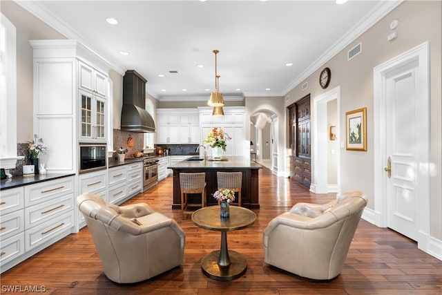 kitchen featuring a center island with sink, wall chimney exhaust hood, decorative light fixtures, and hardwood / wood-style flooring