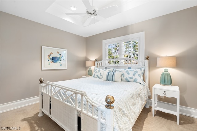 bedroom with light carpet, a raised ceiling, and ceiling fan