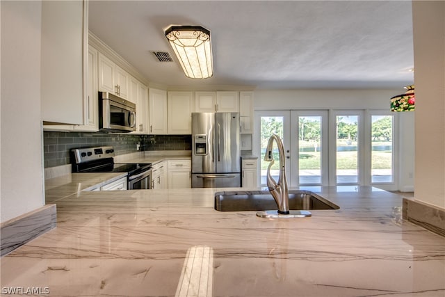 kitchen with white cabinetry, kitchen peninsula, stainless steel appliances, sink, and tasteful backsplash