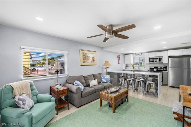 living room with light hardwood / wood-style flooring, a healthy amount of sunlight, and ceiling fan