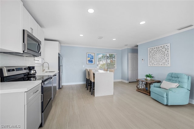 kitchen with appliances with stainless steel finishes, a breakfast bar area, light hardwood / wood-style floors, white cabinetry, and a center island