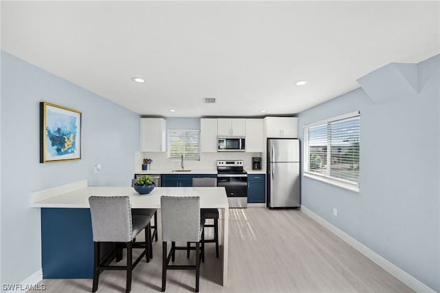 kitchen featuring light hardwood / wood-style floors, a kitchen breakfast bar, appliances with stainless steel finishes, white cabinetry, and sink