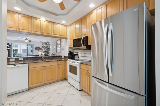 kitchen with ceiling fan, appliances with stainless steel finishes, a tray ceiling, dark stone countertops, and sink