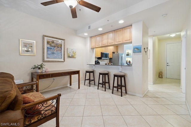 kitchen featuring ceiling fan, a breakfast bar, stainless steel appliances, light tile floors, and light brown cabinetry