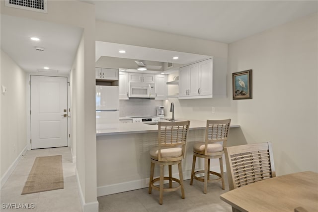 kitchen featuring white cabinetry, a kitchen bar, white appliances, and kitchen peninsula