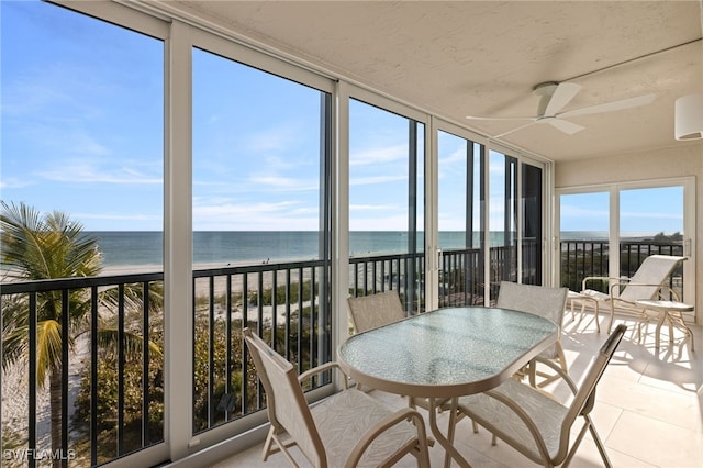 sunroom / solarium with a water view, ceiling fan, and a view of the beach