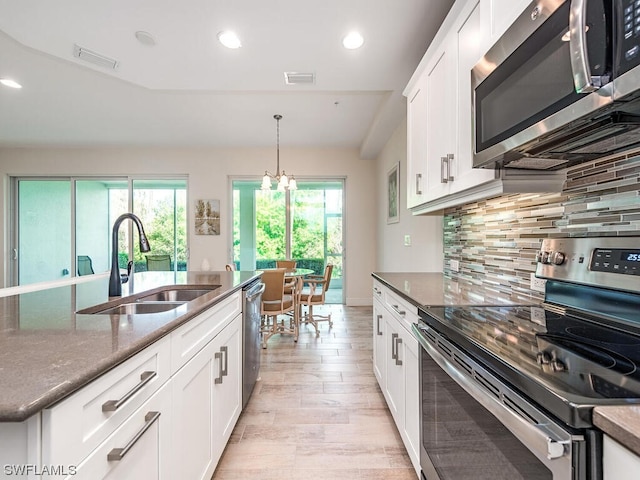 kitchen featuring pendant lighting, decorative backsplash, appliances with stainless steel finishes, sink, and light hardwood / wood-style floors