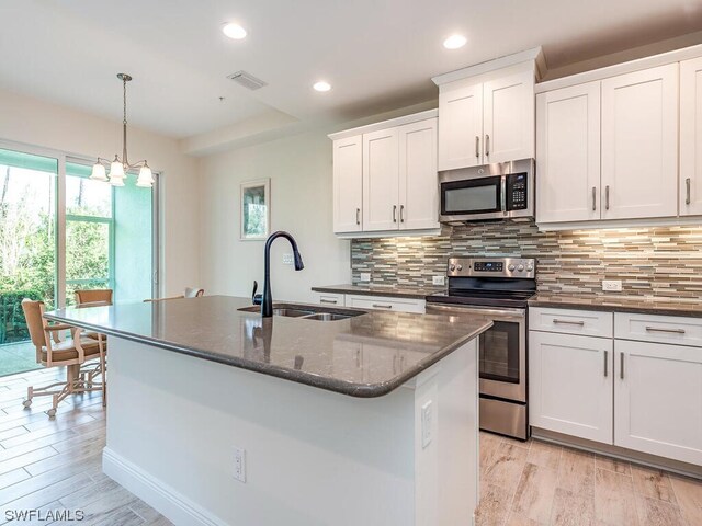 kitchen featuring appliances with stainless steel finishes, decorative backsplash, a center island with sink, and light hardwood / wood-style floors