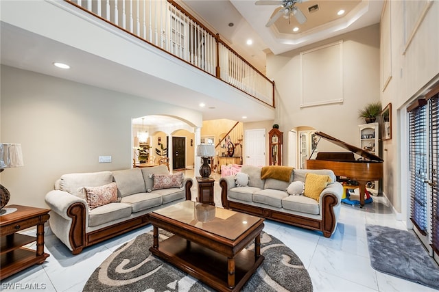 tiled living room with a tray ceiling, ceiling fan, and a towering ceiling