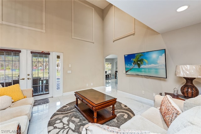 living room with a towering ceiling, light tile floors, and french doors