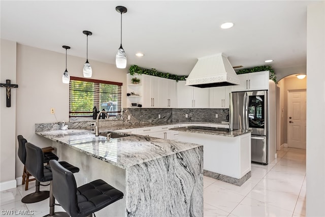 kitchen with light stone counters, tasteful backsplash, white cabinetry, custom range hood, and pendant lighting