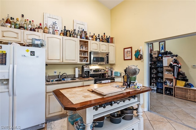 kitchen featuring wood counters, light tile floors, stainless steel appliances, high vaulted ceiling, and sink