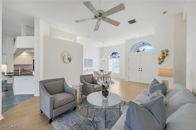 living room with ceiling fan with notable chandelier, light hardwood / wood-style floors, and sink