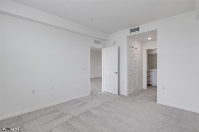 unfurnished bedroom with ensuite bath, light colored carpet, and a closet