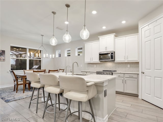 kitchen with white cabinets, appliances with stainless steel finishes, a center island with sink, and hanging light fixtures