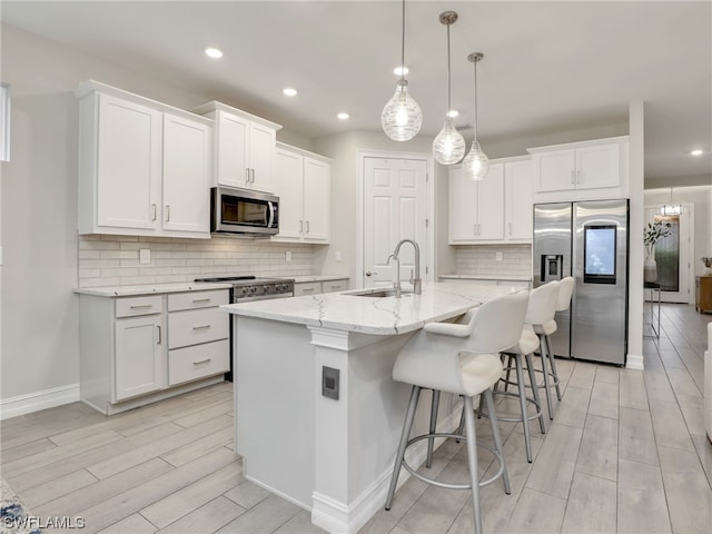 kitchen featuring high end appliances, a kitchen island with sink, white cabinets, sink, and decorative light fixtures